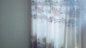 Una habitación con una cortina estampada, piso de baldosas y una pared lisa.