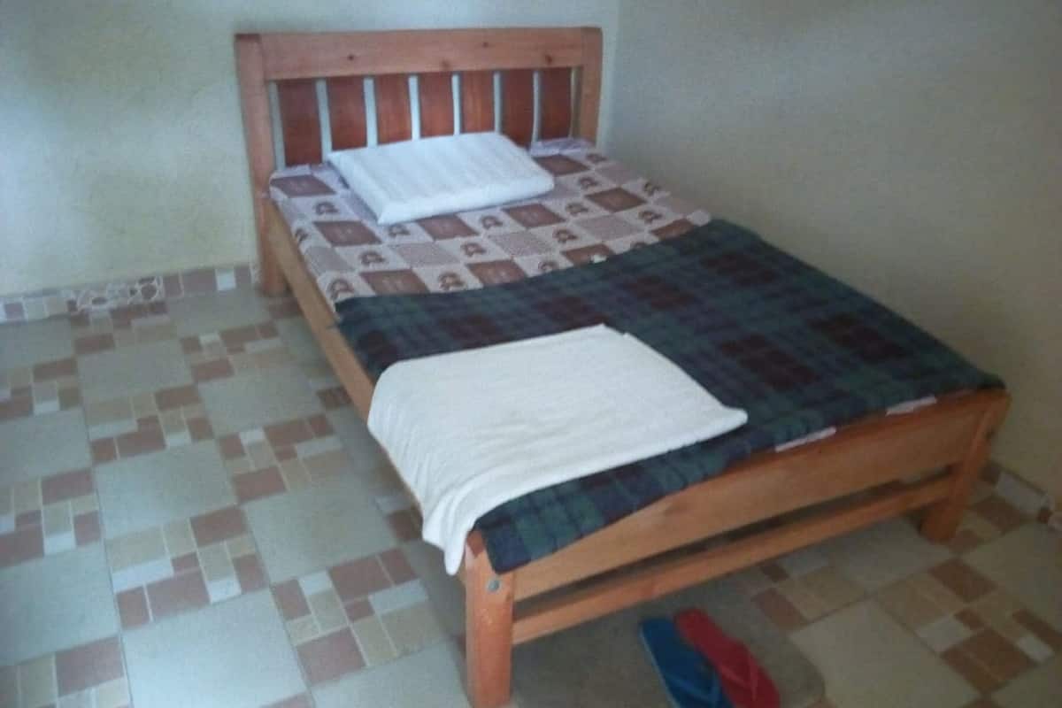 A single bed with a wooden headboard, a patterned bedspread, and a white blanket.