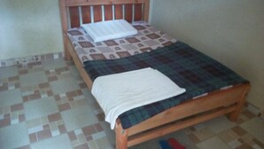 Una cama individual con cabecera de madera, cubrecama estampado y manta blanca.