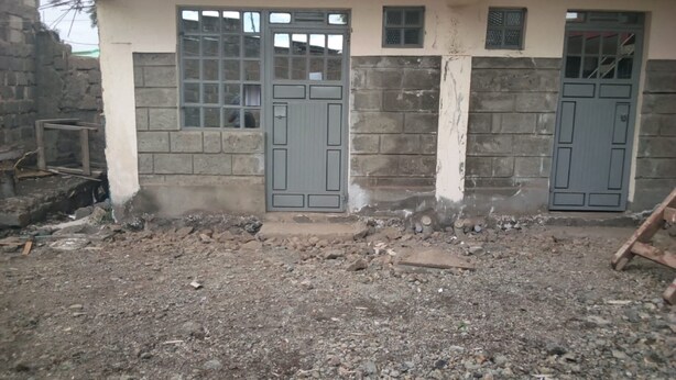 Un edificio con dos puertas grises, ventanas, un tejado rojo y una pared de ladrillo.