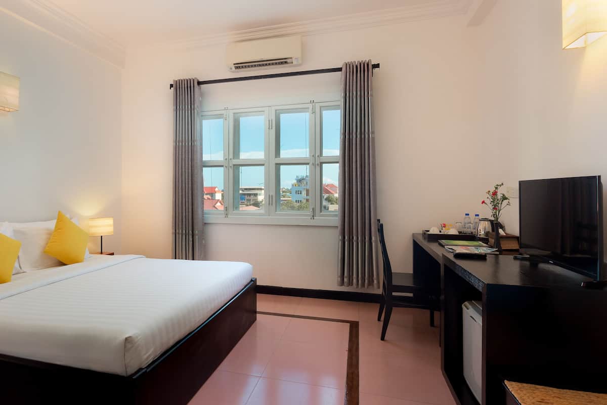 A hotel room with a bed, bedside lamps, a desk with a television, and a window with curtains.