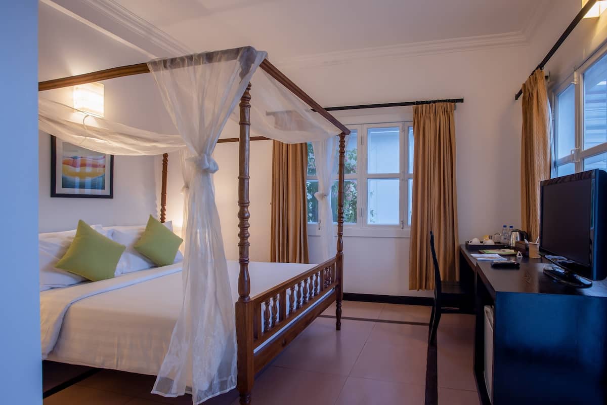 A four-poster bed with a canopy, a desk with a television, and a window with curtains.