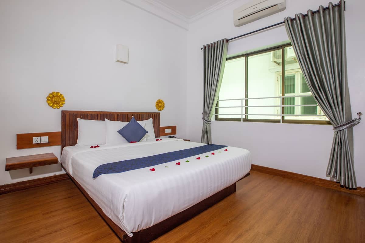 A neatly made bed with a wooden headboard, a bedside table, and a window with curtains.