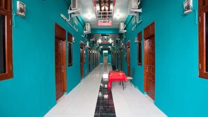 A corridor with teal walls, wooden doors, and a red table with chairs. - OYO 1978 Pondok Indah Residence (Medan)