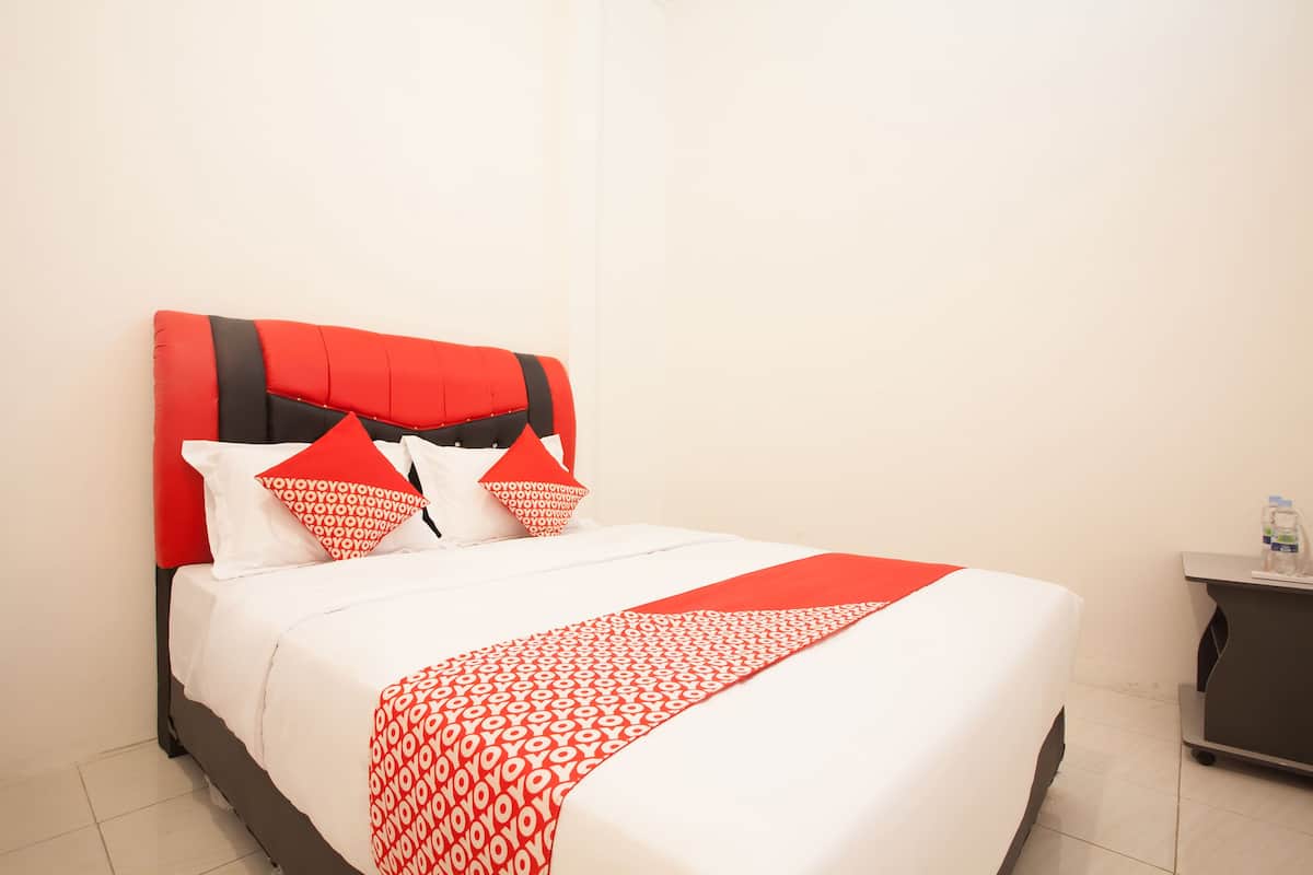 Hotellihuone, jossa on sänky, yöpöytä ja yöpöydällä vesipullo.