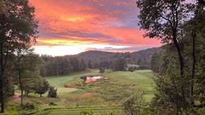 Un parcours de golf avec un étang, entouré d’une forêt dense et illuminé par le ciel au coucher du soleil.