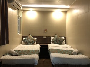A small, narrow hotel room with two single beds, each with a pillow and a rolled towel. There is a window on one side and a wall-mounted air conditioner above it. - Starry Inn (Kowloon)