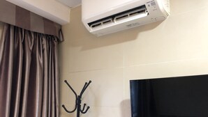 A room with a flat-screen TV, an air conditioning unit, and a coat rack. - Starry Inn (Kowloon)