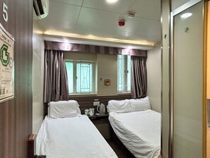 A hotel room with two single beds, a small table with a kettle, and a window with curtains. - Starry Inn (Kowloon)