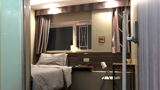 A compact bedroom with a bed, a small table, a chair, a window, and a wall-mounted ladder. - Starry Inn (Kowloon)