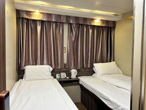 A hotel room with two single beds, a small table with a kettle and a remote control, and a window with curtains. - Starry Inn (Kowloon)