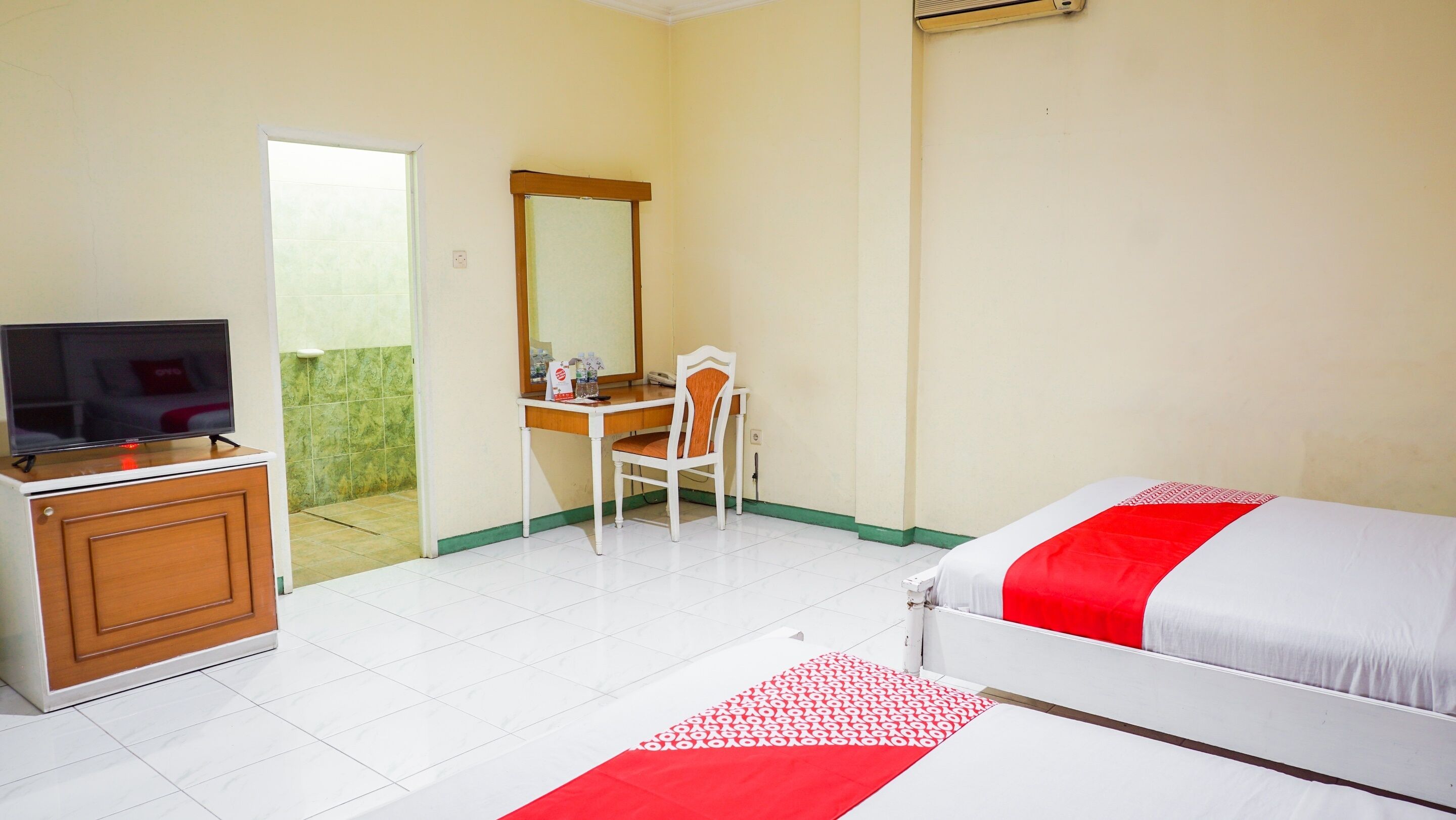 Habitación de hotel con cama, escritorio con silla, televisor en un mueble y baño visible a través de una puerta abierta.