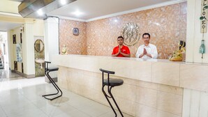 A hotel reception area with a marble wall, a reception desk, two bar stools, and a statue of a woman. - OYO 2085 Chrysanta Hotel (Bandung)