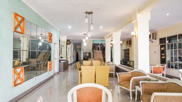 A spacious lobby with a central seating area, a staircase, and a glass wall with orange frames. - OYO 2085 Chrysanta Hotel (Bandung)
