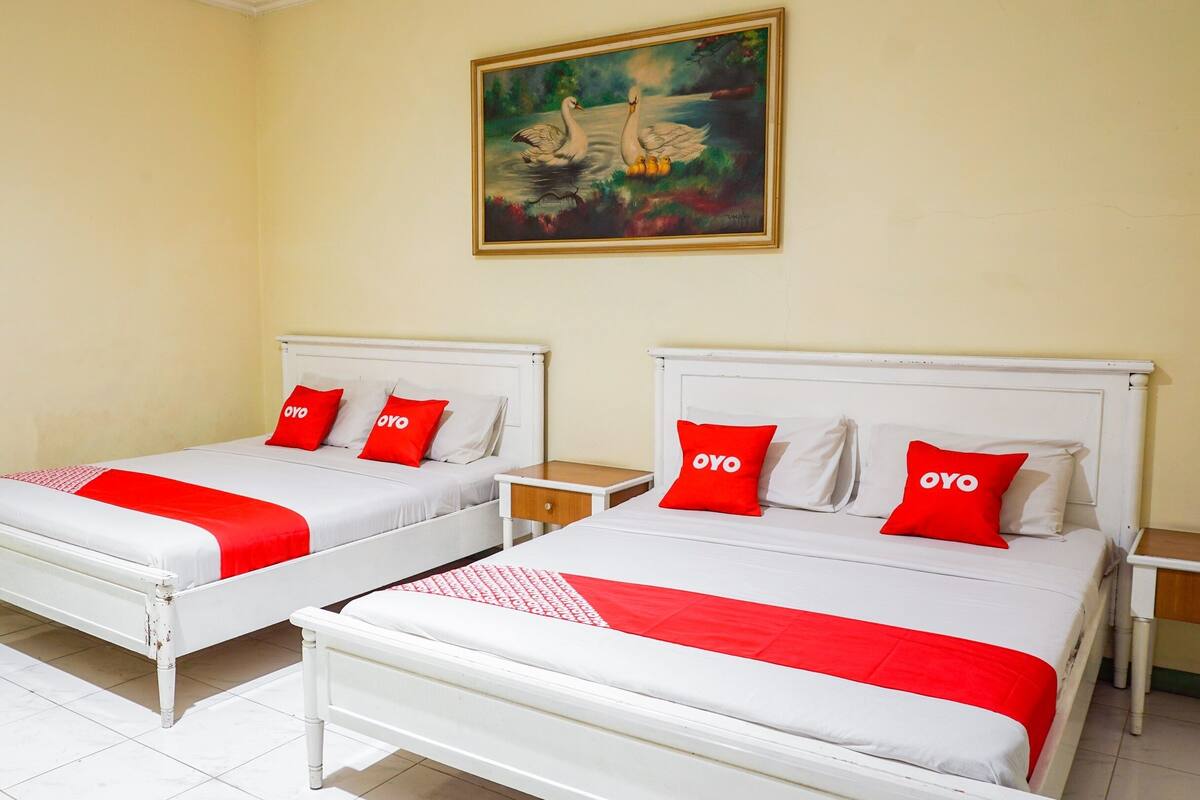 Two single beds with white frames and red bedding, a small wooden nightstand, and a painting of swans on the wall.