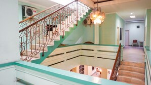 A staircase with ornate metal railings and a chandelier, leading to a lower level with a view of the interior. - OYO 2085 Chrysanta Hotel (Bandung)