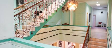 A staircase with ornate metal railings and a chandelier, leading to a lower level with a view of the interior.