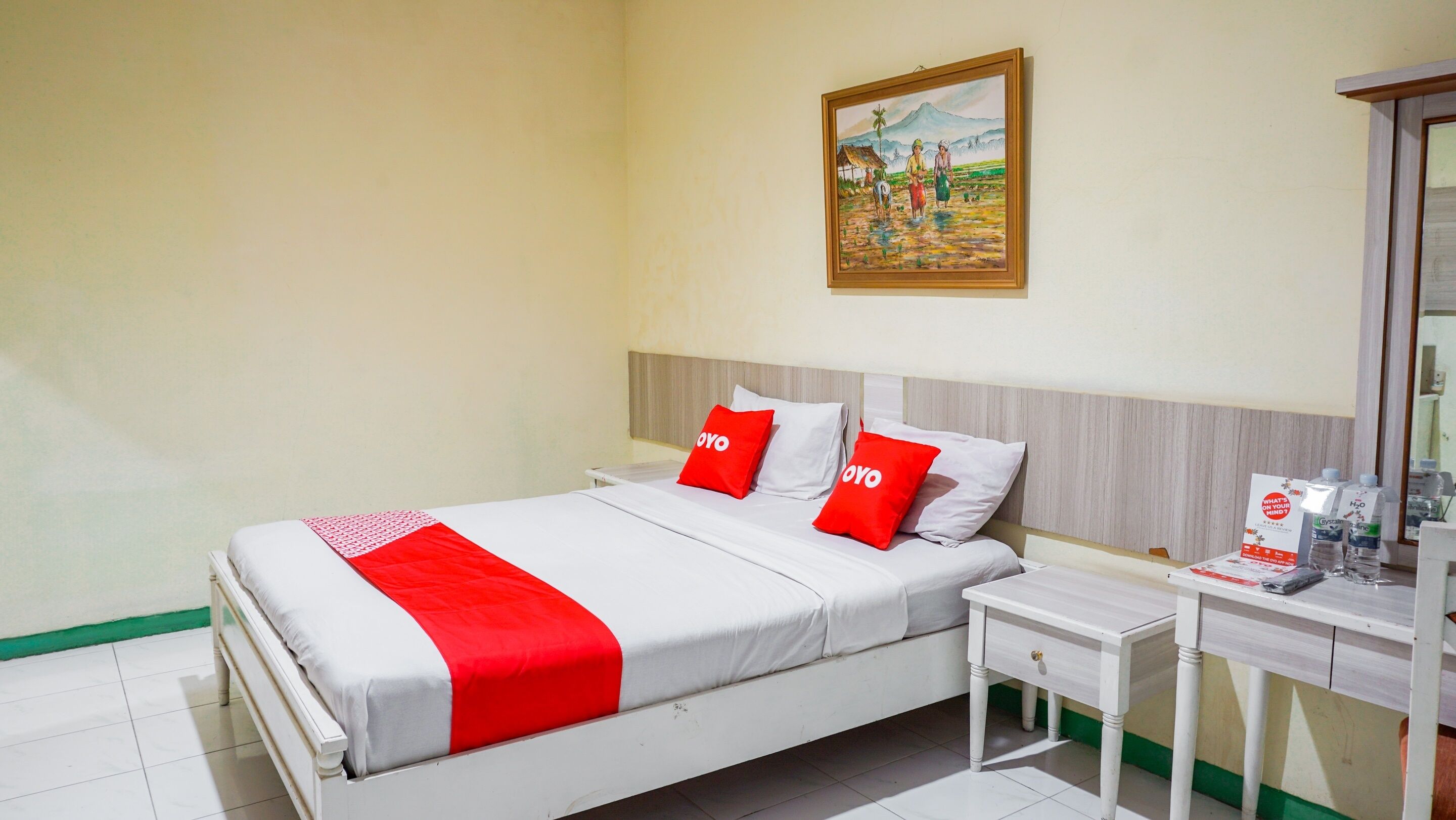Een hotelkamer met een bed, nachtkastje, en een schilderij aan de muur.