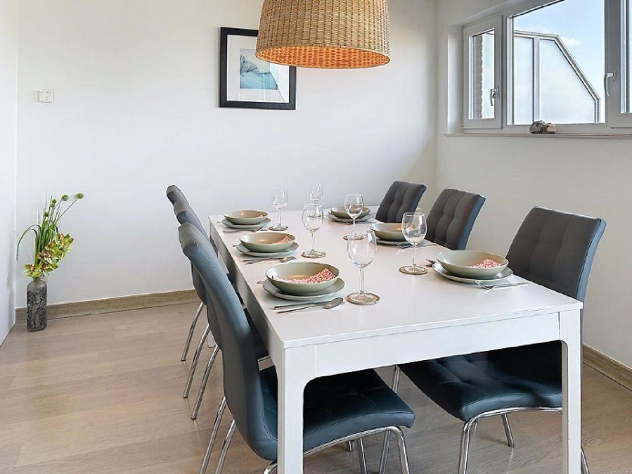 A dining area with a white table, black chairs, and a woven pendant light.
