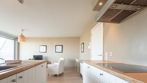 Een moderne keuken met witte kasten, een houten aanrecht en een inbouwfornuis. Er is een eethoek met een witte stoel en een tafel.
