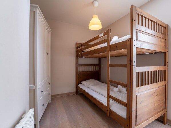 Een slaapkamer met een stapelbed met houten frame, een witte garderobe en een hanglamp.