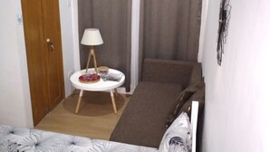 A bedroom with a bed, a small table with a chair, a wooden door, and a window with curtains. - Homeystay 2 (Lapu-Lapu)