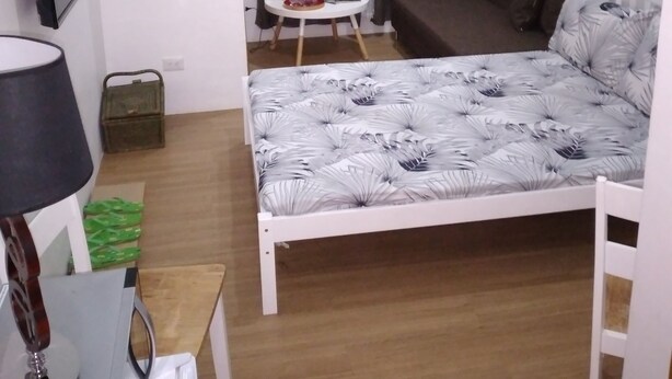 A compact bedroom with a single bed, a small table, a lamp, a TV, and a window with curtains. - Homeystay 2 (Lapu-Lapu)