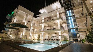 A multi-story hotel with a pool area, outdoor seating, and a staircase leading to the upper floors. - Rovira Suites (Dumaguete)
