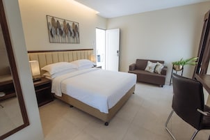 A hotel room with a bed, a sofa, a chair, and a wall-mounted artwork.
