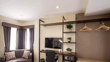 Een moderne hotelkamer met een bank, een bureau met een computer, een televisie en een wandplank met planten en kapstok.