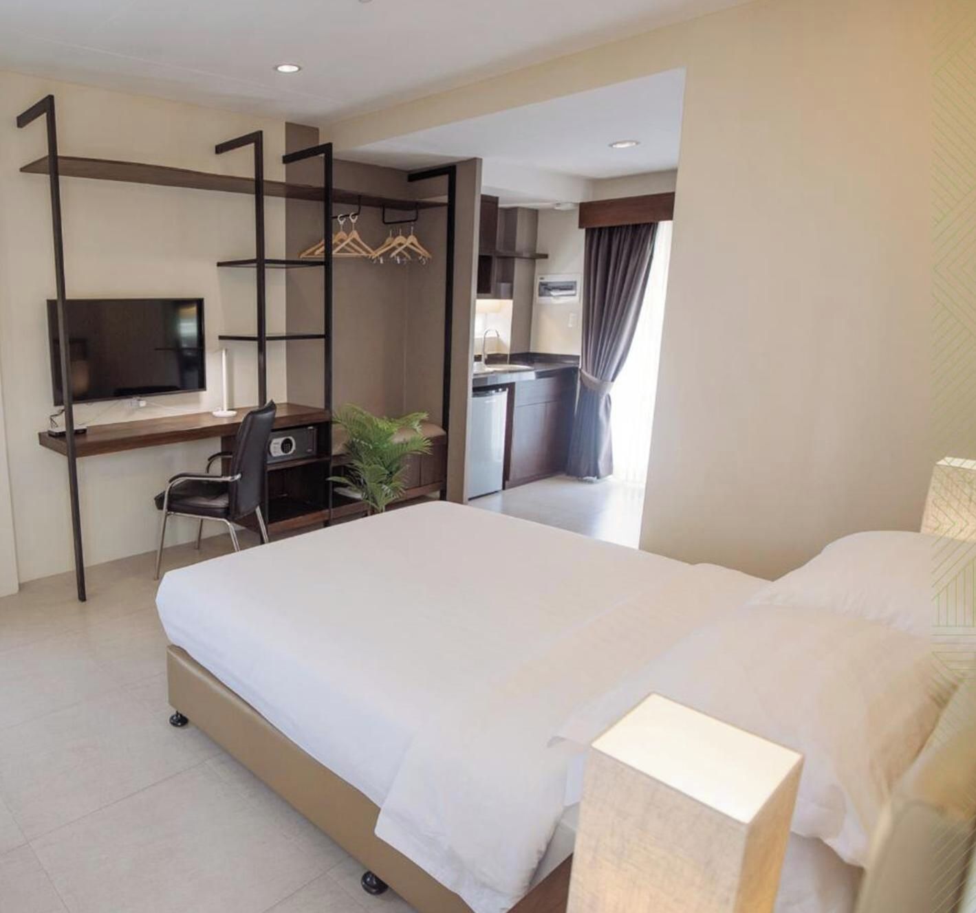 Habitación de hotel con cama, escritorio con computadora, televisor y una pequeña planta.