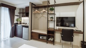 A modern kitchen with a built-in dishwasher, a dining area with a bench, a TV mounted on a wooden shelf, and a black chair. - Rovira Suites (Dumaguete)