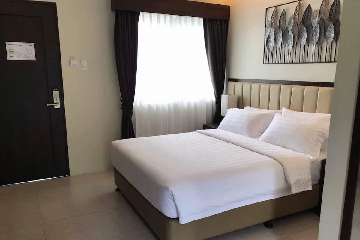 A hotel room with a bed, curtains, a wall-mounted artwork, and a door.
