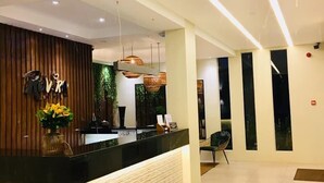 A modern reception area with a wooden reception desk, a plant, and a hanging light fixture. - Rovira Suites (Dumaguete)