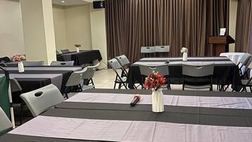 Un salón de conferencias con mesas, sillas, un proyector y cortinas.