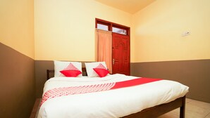 A neatly made bed with white and red bedding, a wooden headboard, and a red door in the background. - OYO 1378 Tengger Indah Homestay (Ngadisari)
