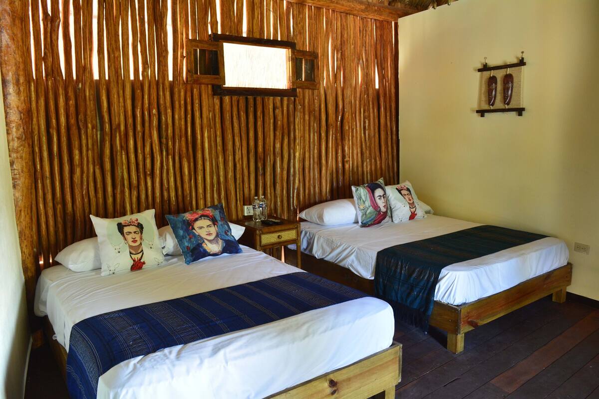 Two single beds with wooden frames and white bedding, a small bedside table with a lamp, and a wooden wall paneling.