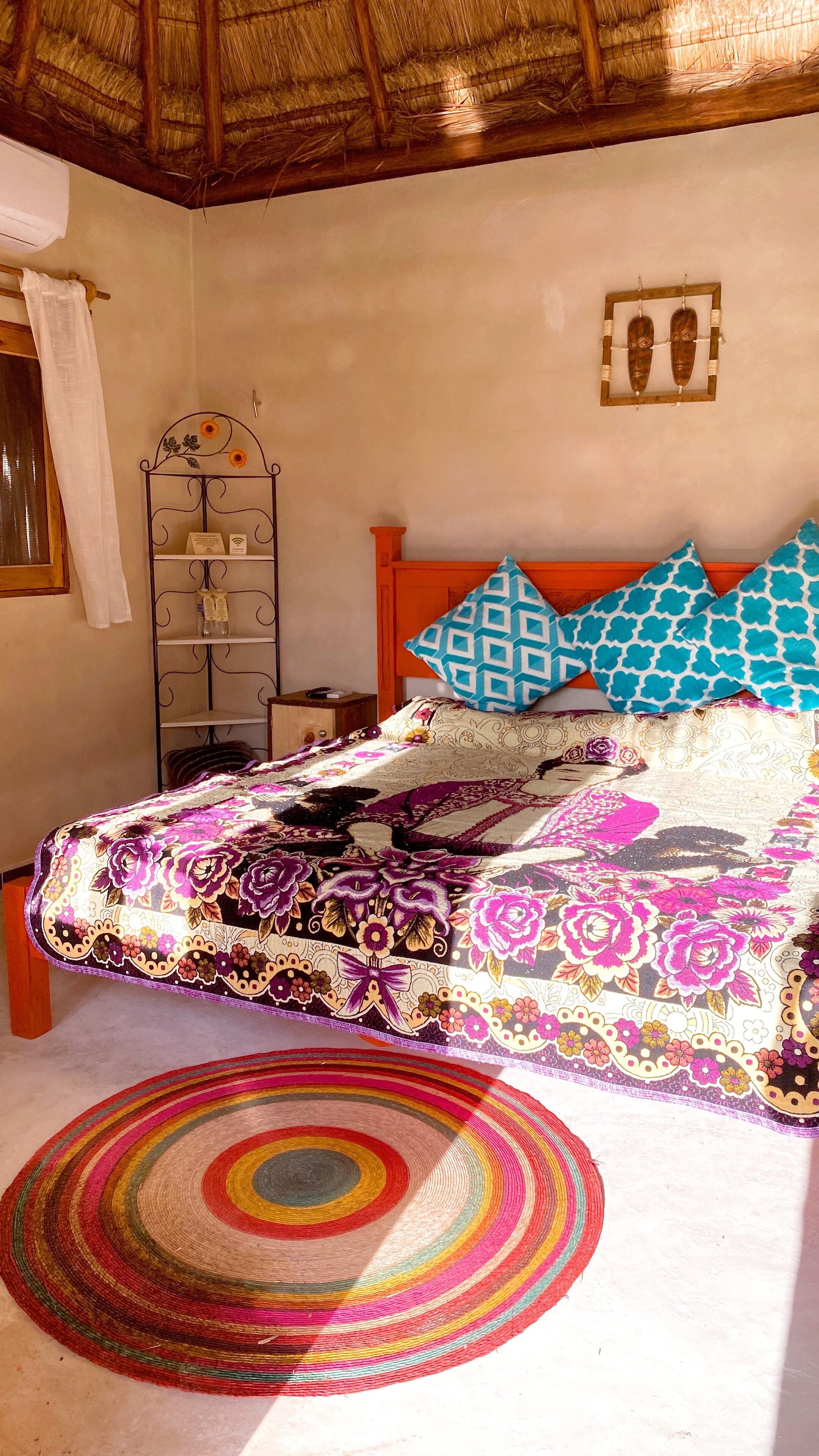 Una cama con una colorida colcha estampada, un cabecero de madera y dos almohadas con diseños.