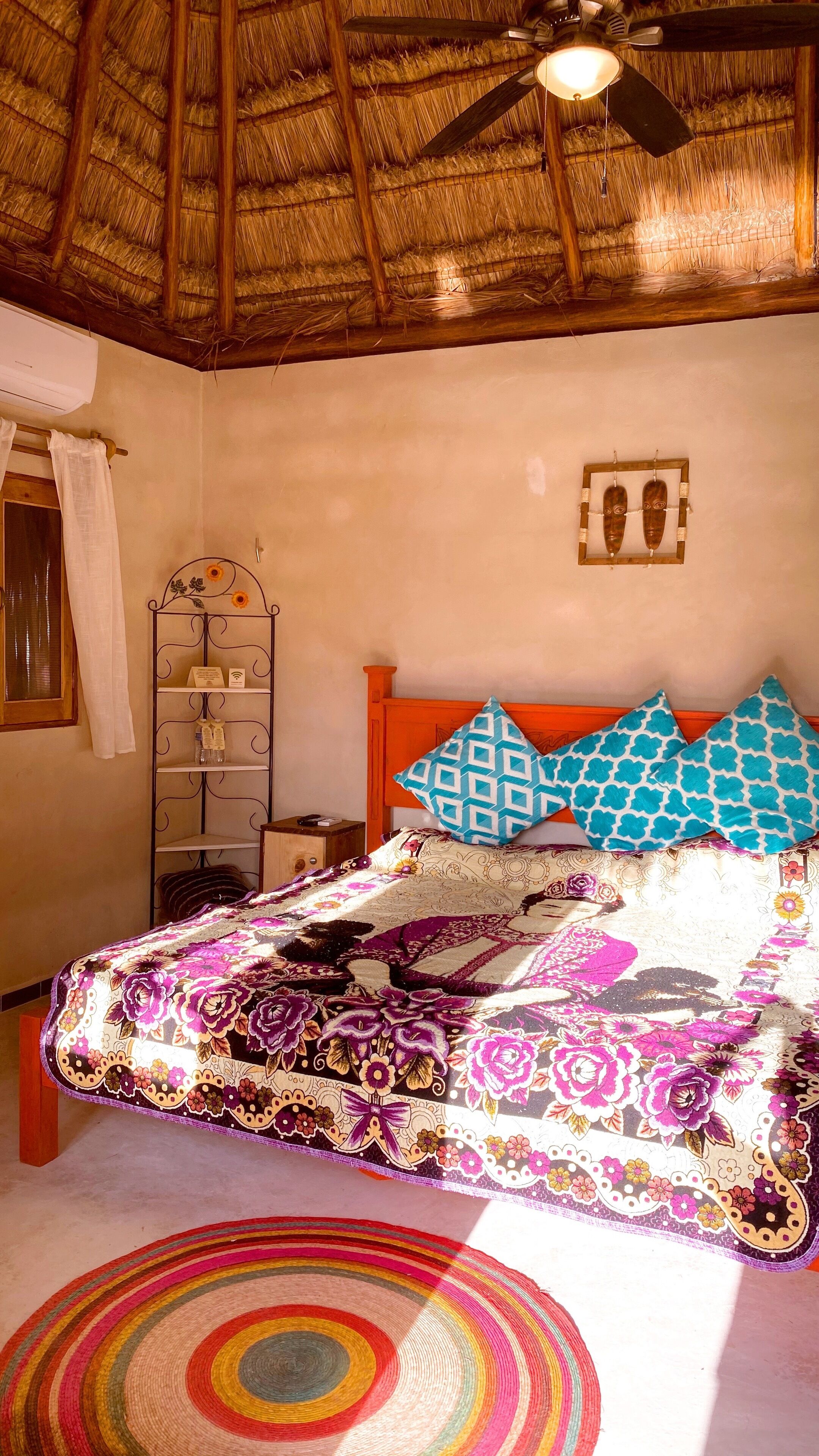 A room with a bed, a ceiling fan, a shelf with toiletries, and a wall-mounted picture.
