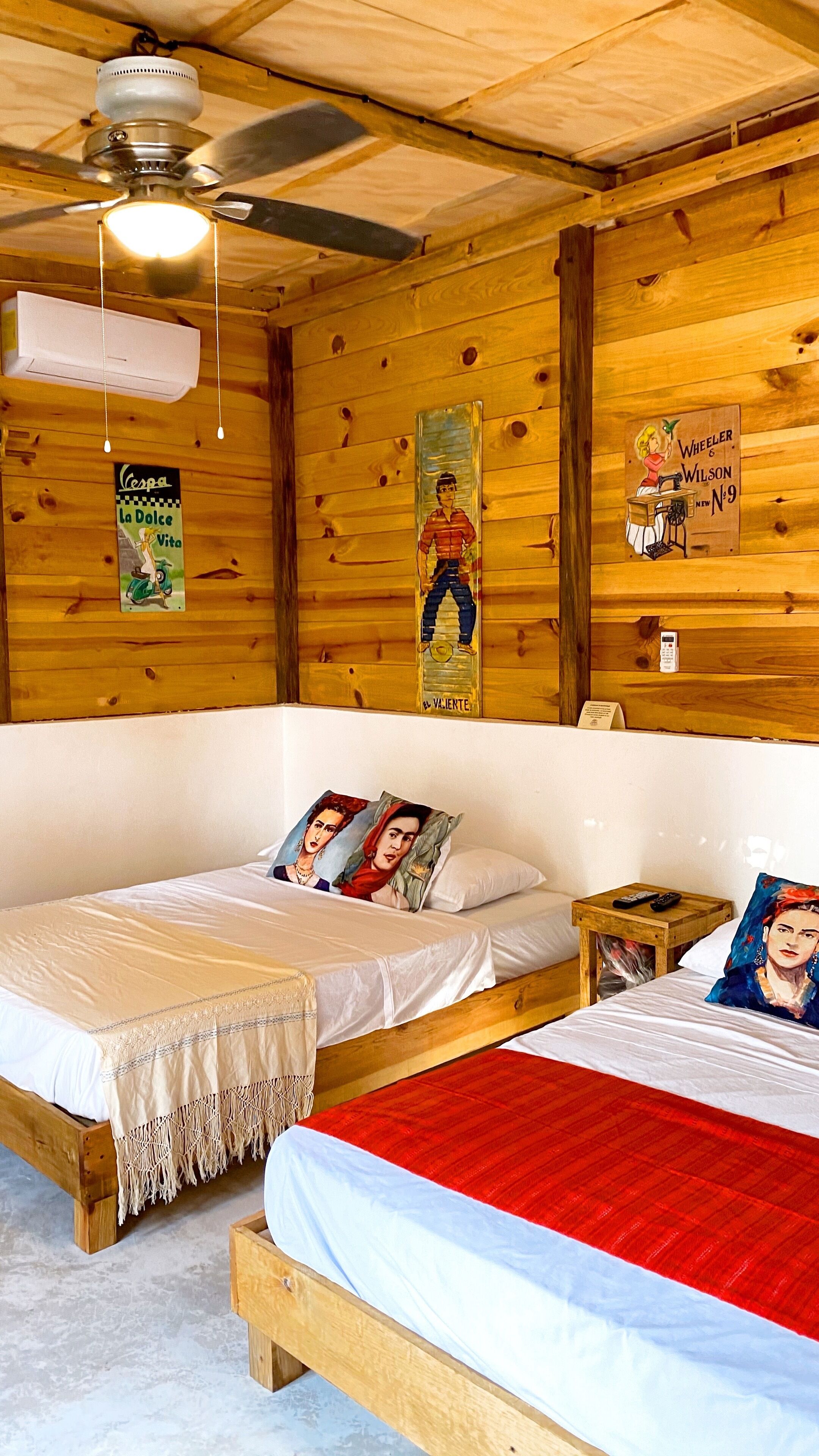 A wooden cabin room with two beds, a ceiling fan, and wooden walls.