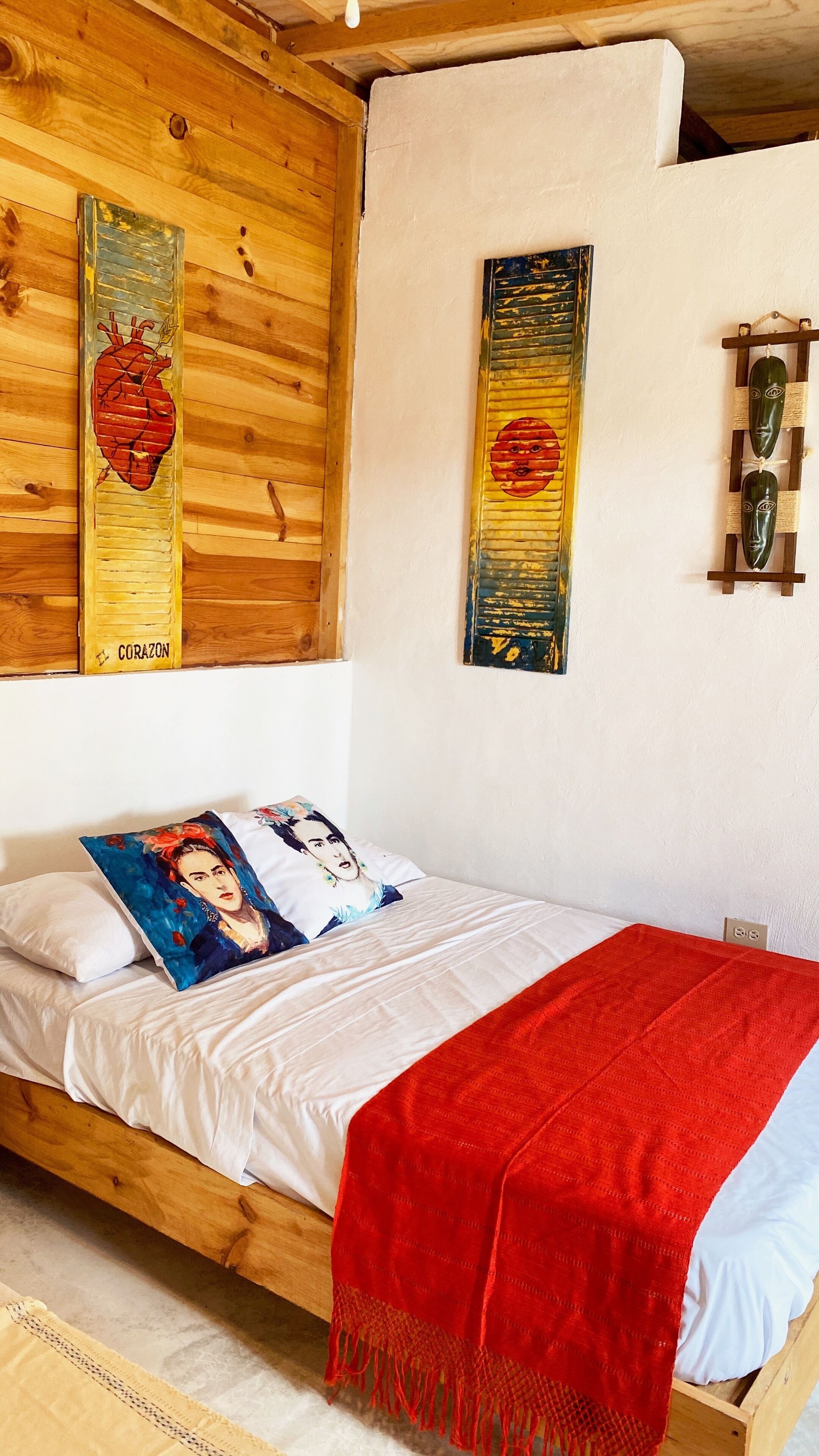A single bed with a red blanket, white bedding, and a pillow with a blue and white design.