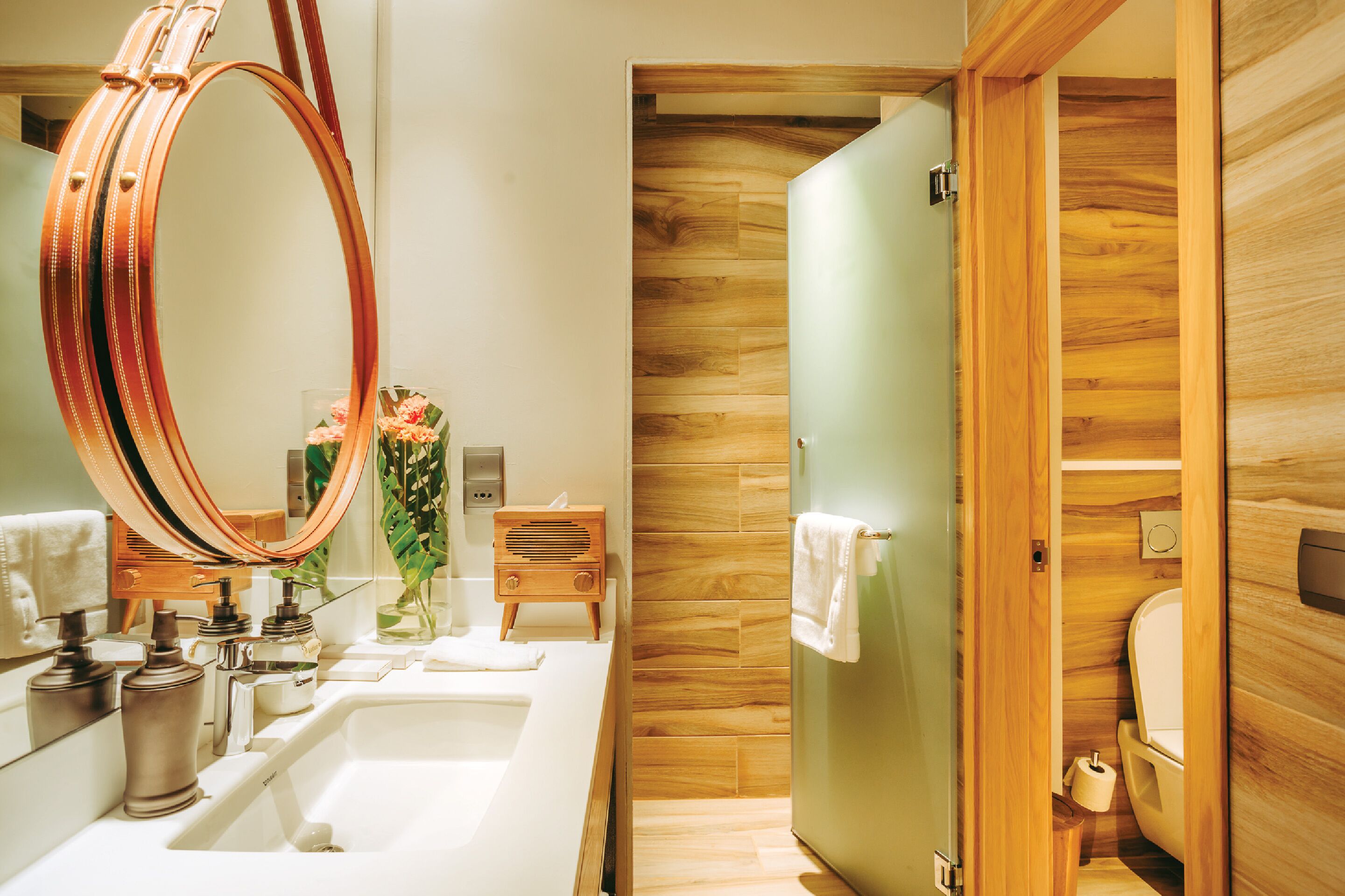 Un baño moderno con un espejo grande, lavamanos dobles, un mueble de tocador de madera y un área separada para el inodoro.