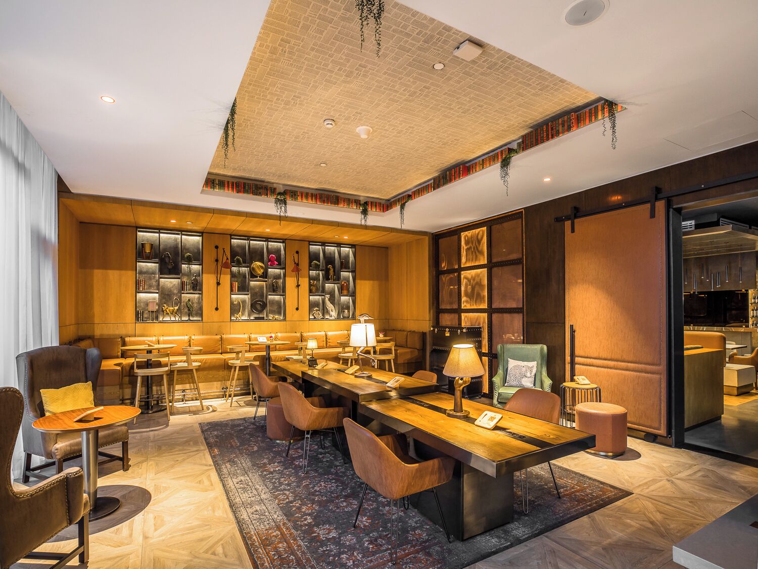 A modern hotel lobby with a long reception desk, leather seating, and a large bookshelf.