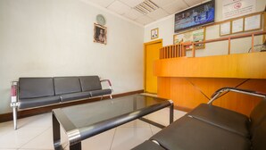 Un área de espera con un banco, una mesa de vidrio, un mostrador de madera y un televisor en la pared.