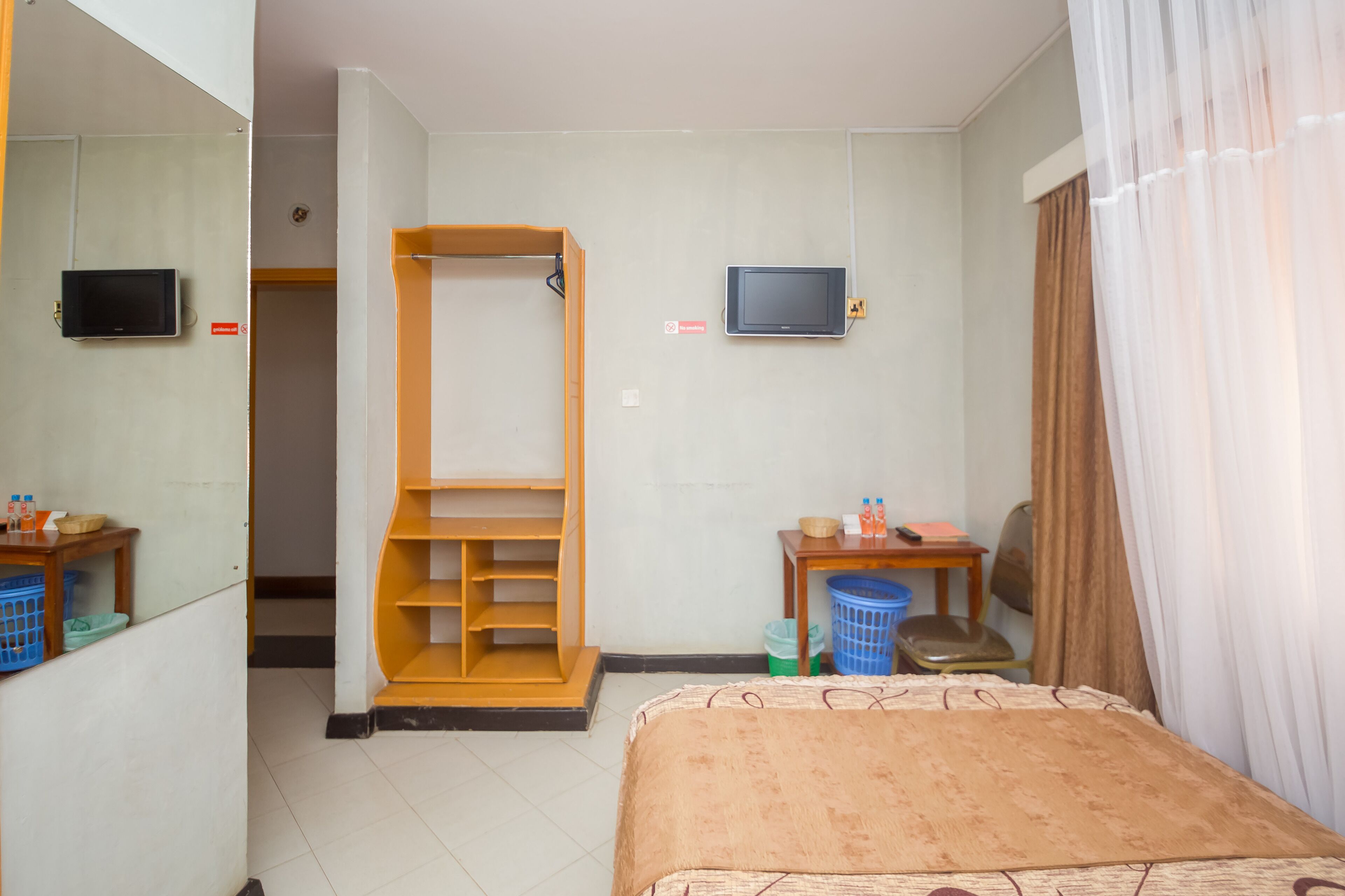 A hotel room with a bed, a television, a wardrobe, a desk with a chair, and a window with curtains.