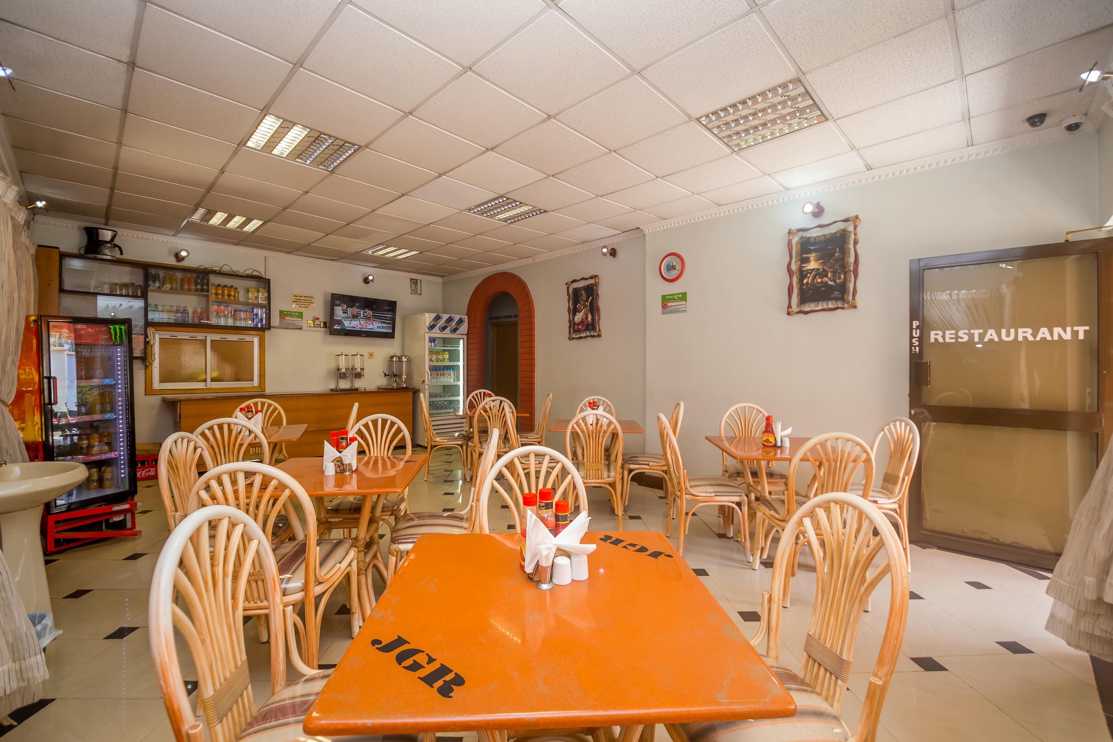 A restaurant interior with wooden chairs, tables, a refrigerator, and a menu board.