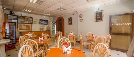 A restaurant interior with wooden chairs, tables, a refrigerator, and a menu board.