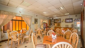 Un restaurante con varias mesas y sillas, un televisor en la pared y un refrigerador al fondo.