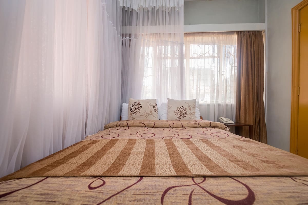 A bedroom with a bed, curtains, and a bedside table with a phone.