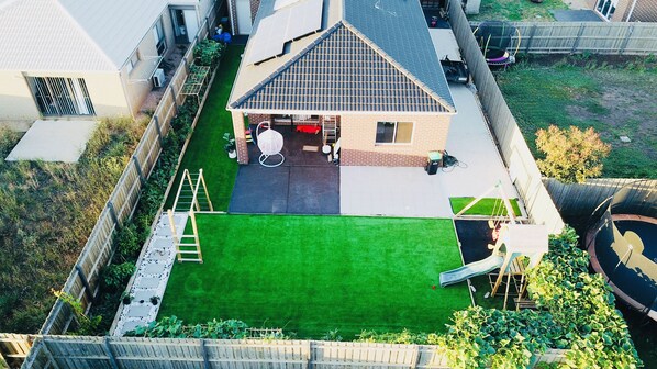 Enjoy a serene backyard with a lush lawn, a shed, and a trampoline, surrounded by a paved driveway and a fence.
